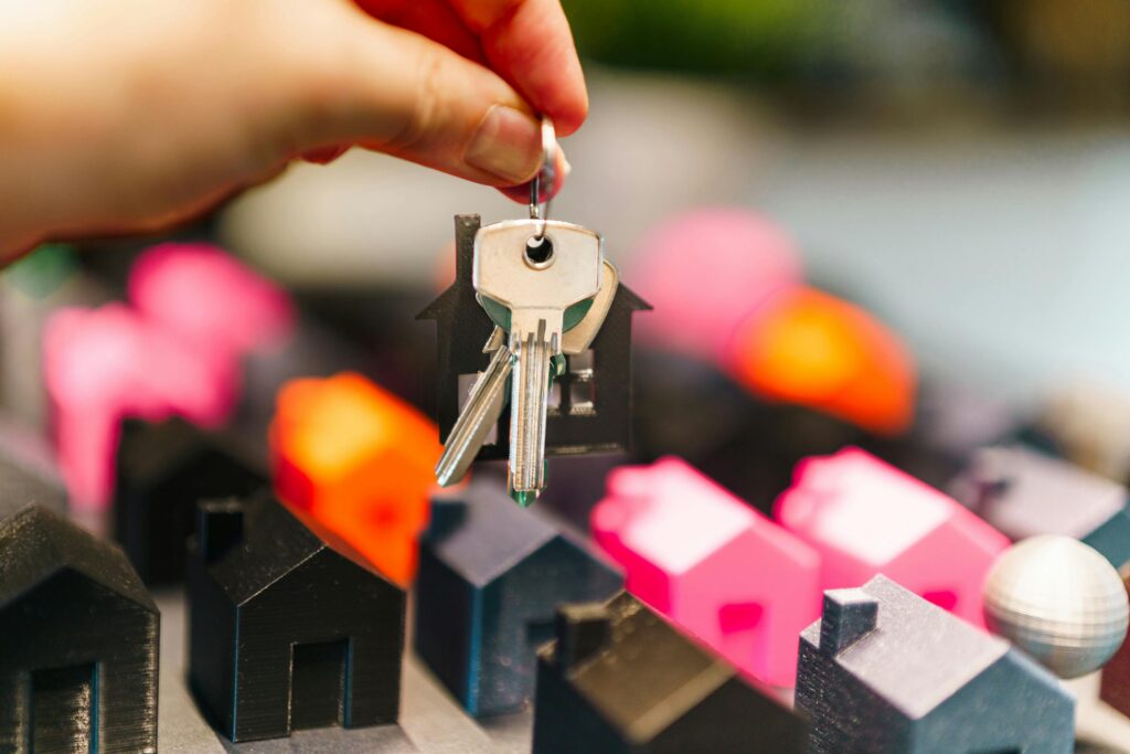 Colorful miniature houses and a hand holding keys representing real estate decisions.